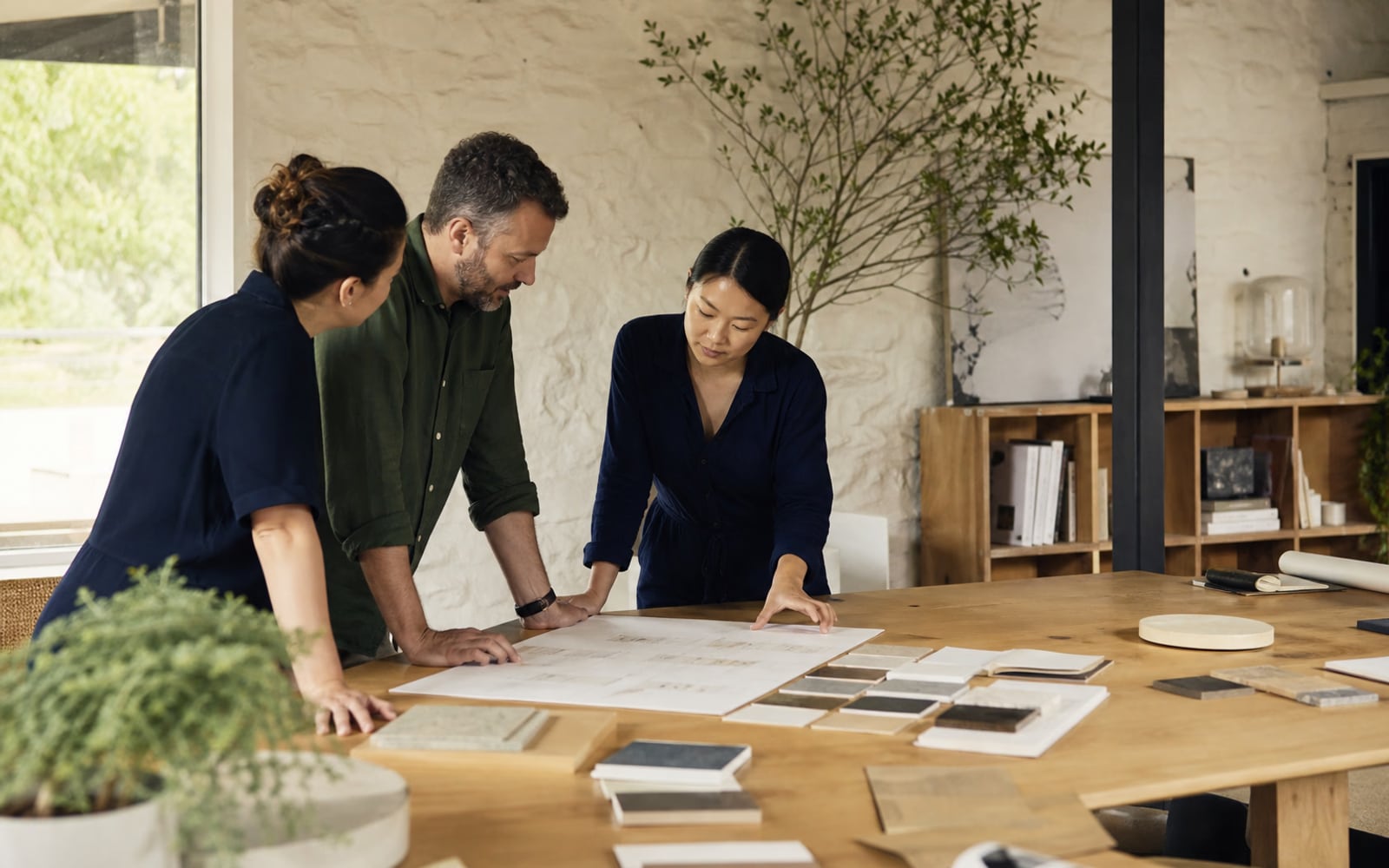 Three colleagues reviewing a shared workflow and material samples around a worktable.